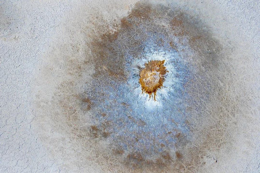 Close-up of a rusty metal surface with a central hole and cracked surrounding paint.