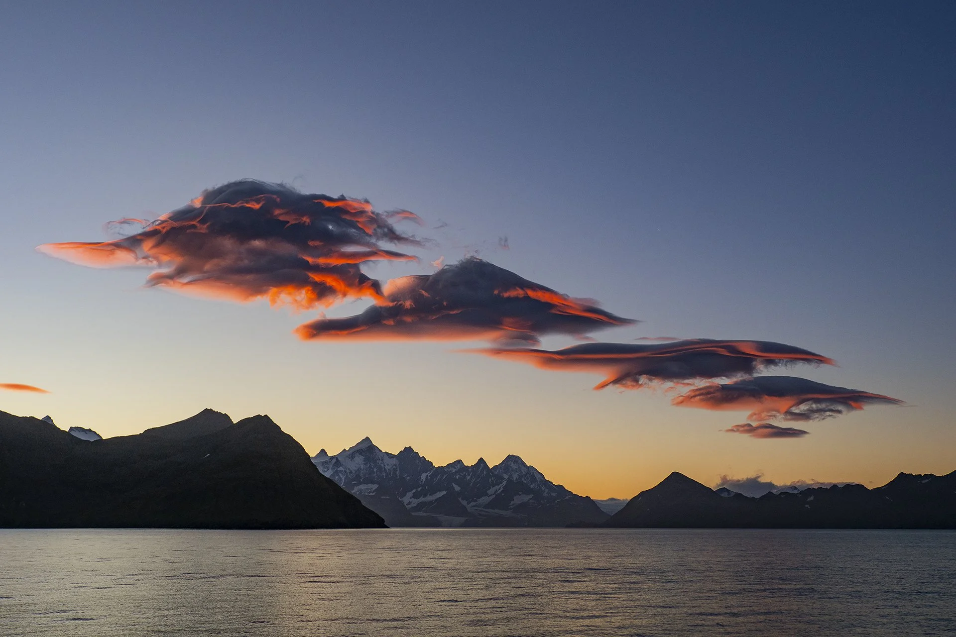Sunset over Antarctica with dramatic clouds reflected across calm polar waters.