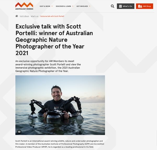 Photograph of Scott Portelli waist-deep in water holding a camera with drone arms, smiling, with a calm ocean and cloudy sky background.