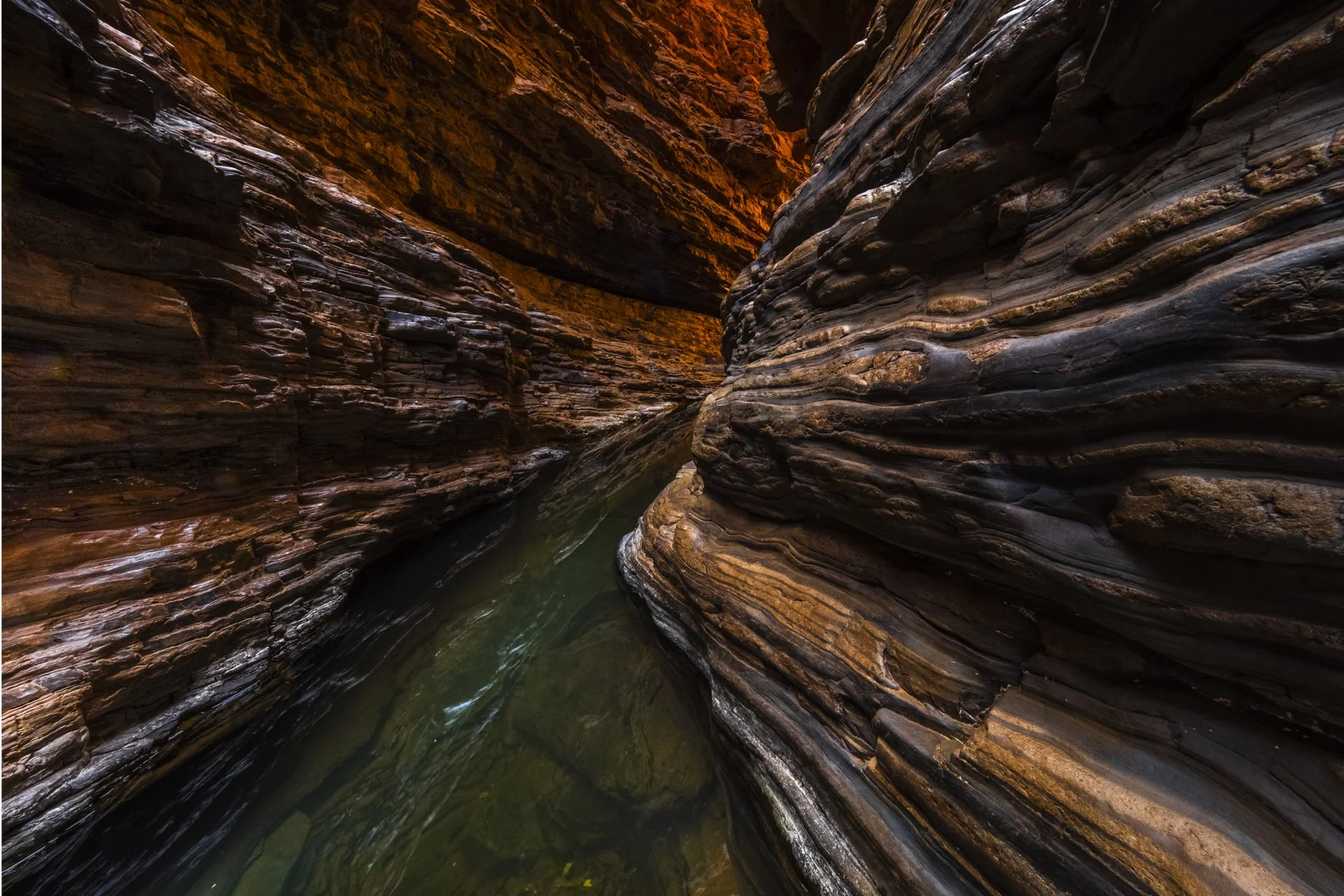Inside a narrow canyon with layered, curved rock walls and a small waterway running through.