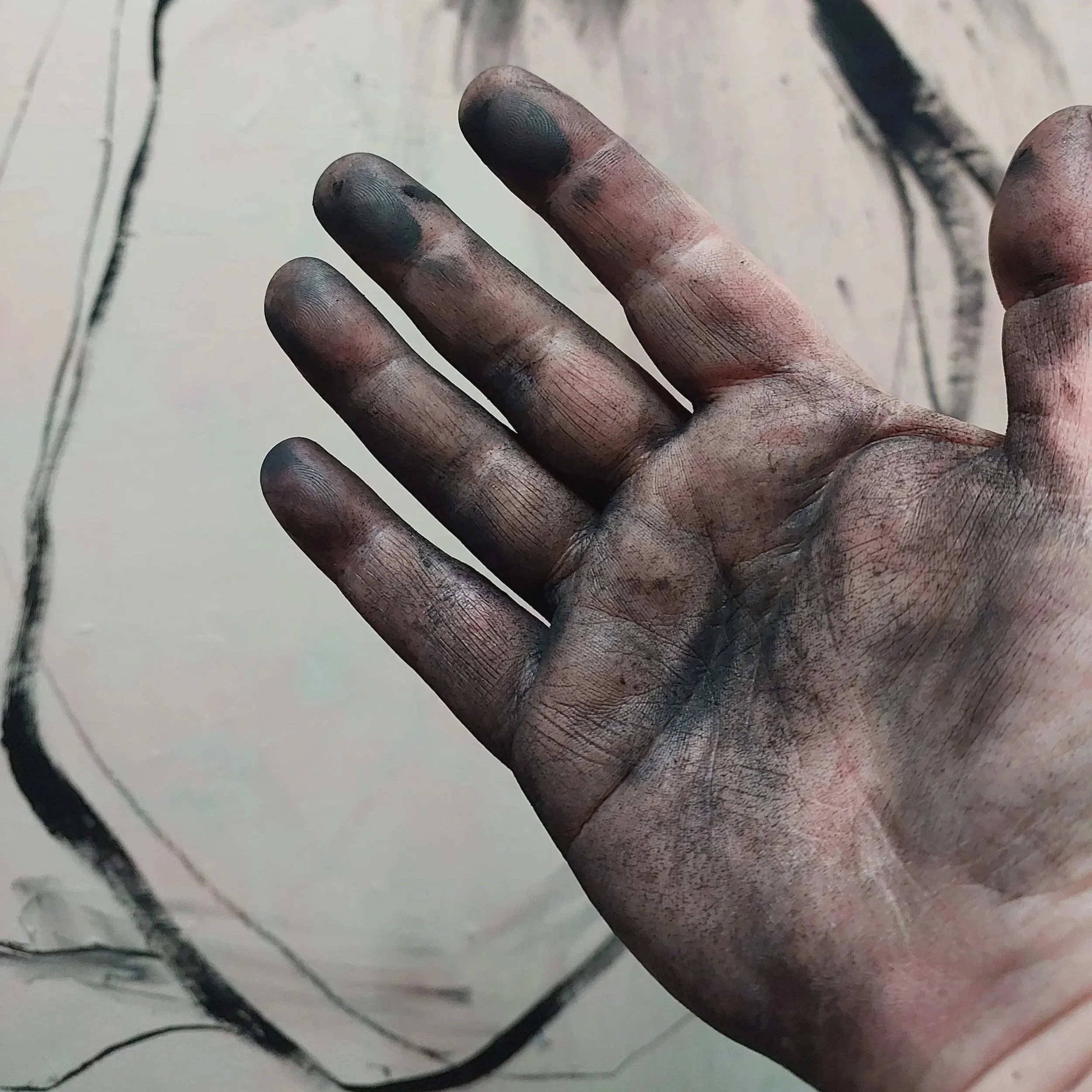 Charcoal-covered hand of artist Lu Bennett in the studio with a figurative drawing in progress behind it.