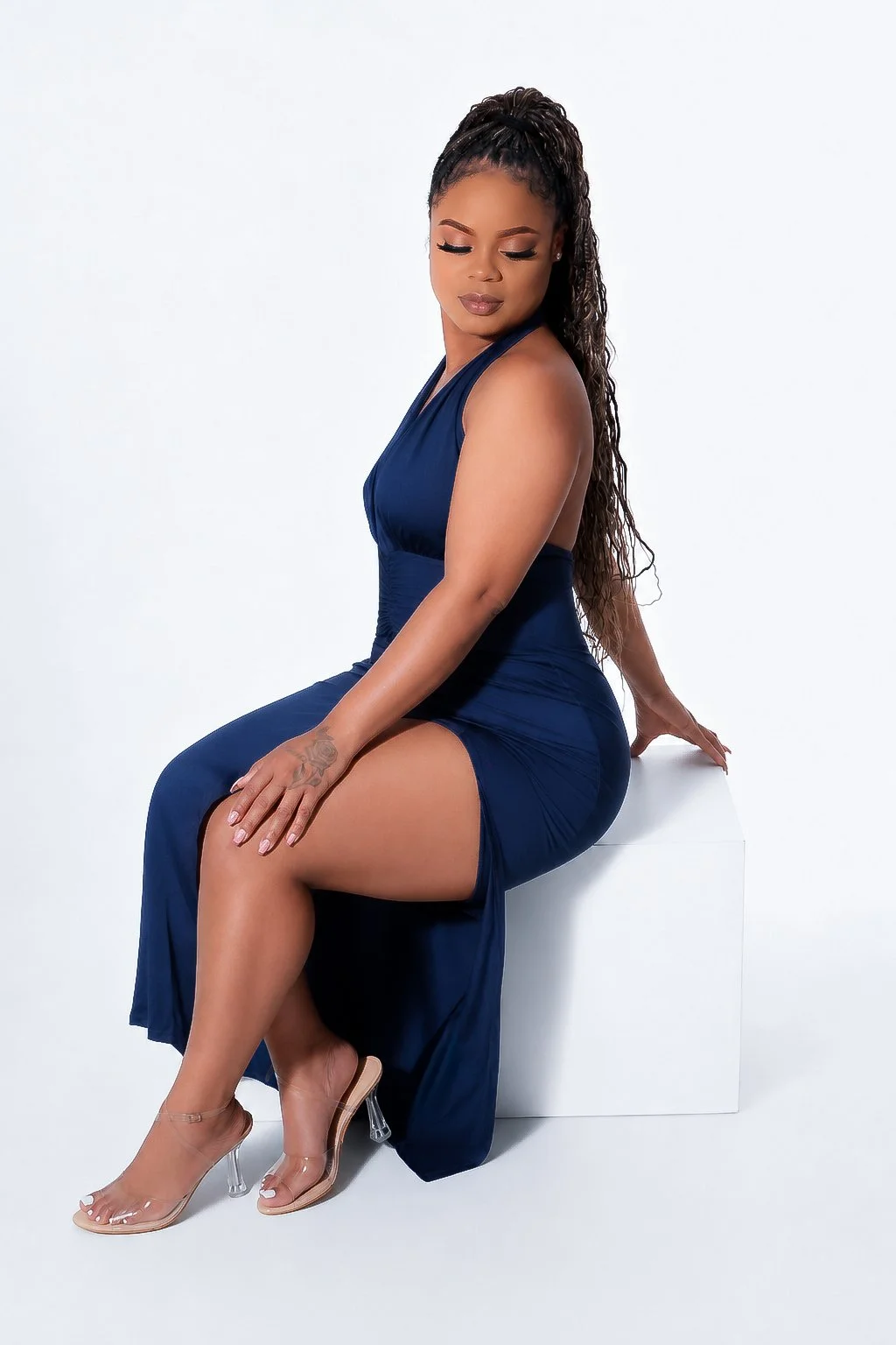 A woman in a navy blue dress sitting on a white block with her eyes closed and hands resting on her knee and the block.