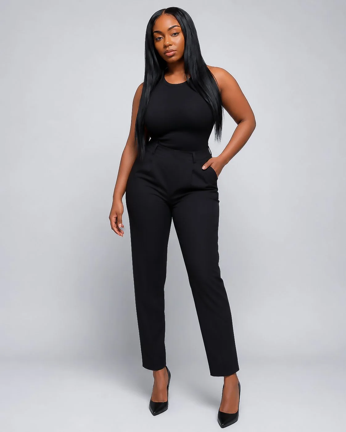 A young woman with long black hair wearing a sleeveless black top, black pants, and black high heels posing against a plain gray background.