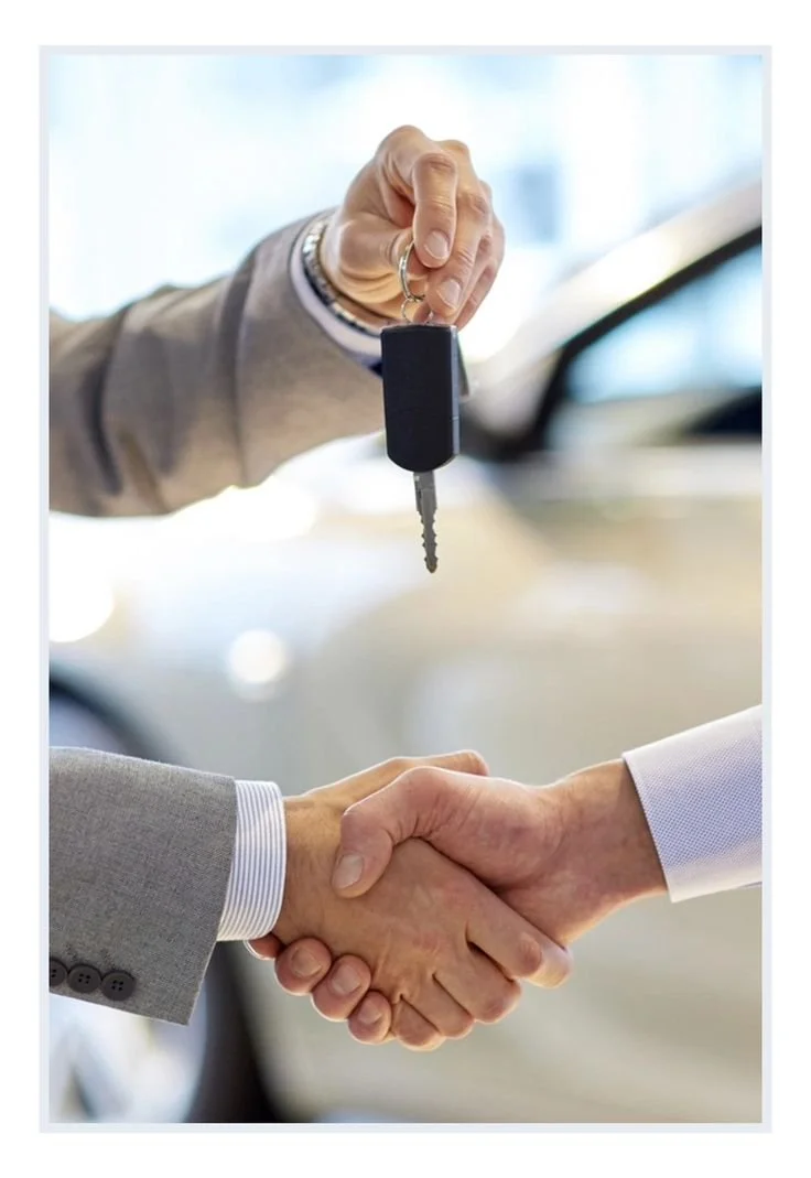 Two people in business suits shaking hands while one is handing over a car key.