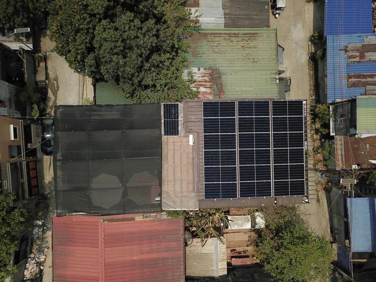 A rooftop with solar panels, shaded area with umbrellas, and surrounding buildings with corrugated metal roofs.