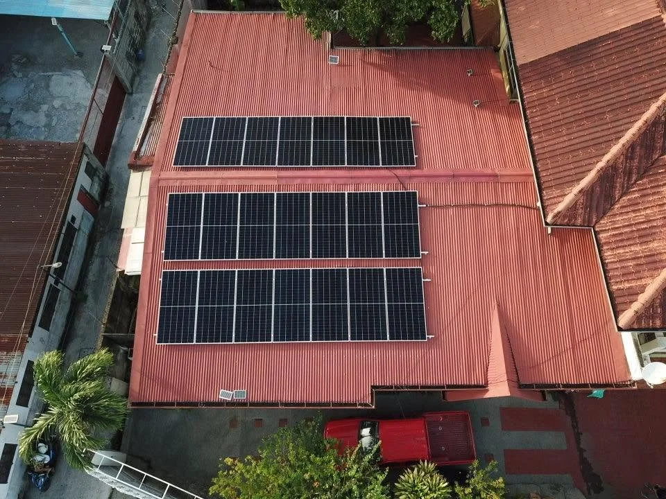 An aerial view of a red metal roof with multiple solar panels installed.