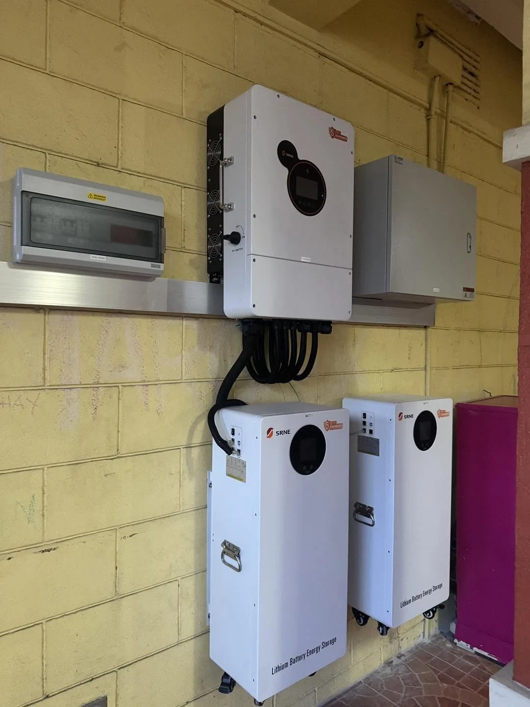 Electrical equipment including a lithium battery energy storage system and an inverter installed on a yellow brick wall.