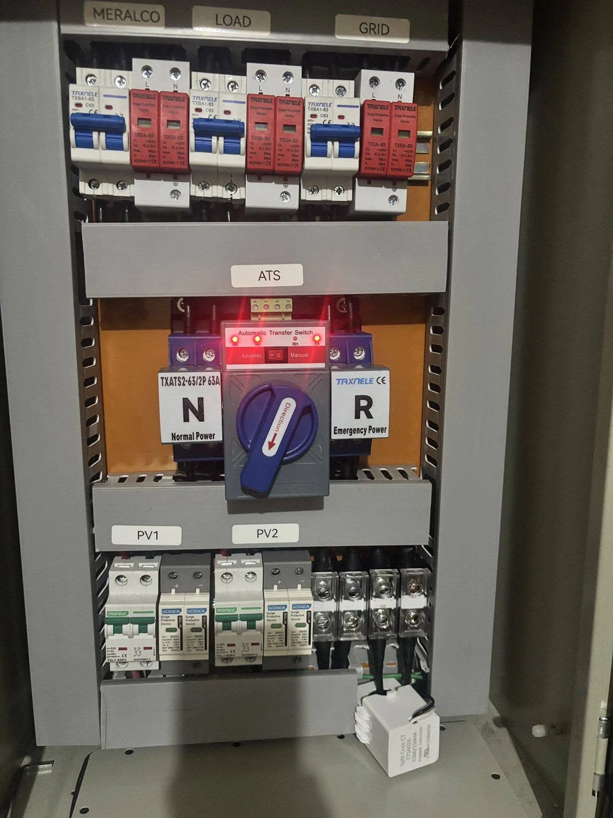 Electrical control panel with circuit breakers labeled MERALCO LOAD GRID, a central switch labeled ATS with a blue dial turned to the right, visible wiring, and wiring terminals at the bottom.