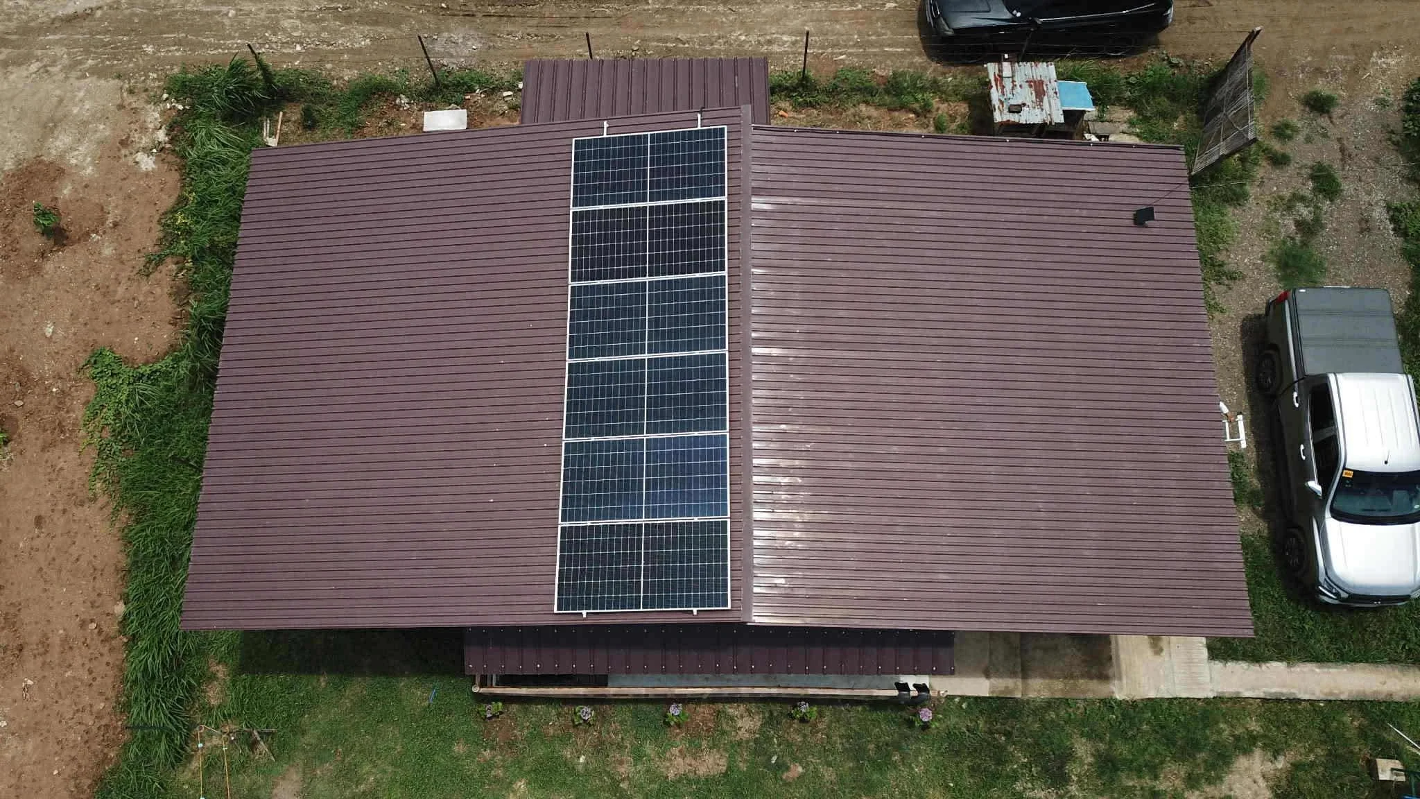 An aerial view of a house with solar panels on the roof, a surrounding yard with some plants, and a driveway with two parked cars.