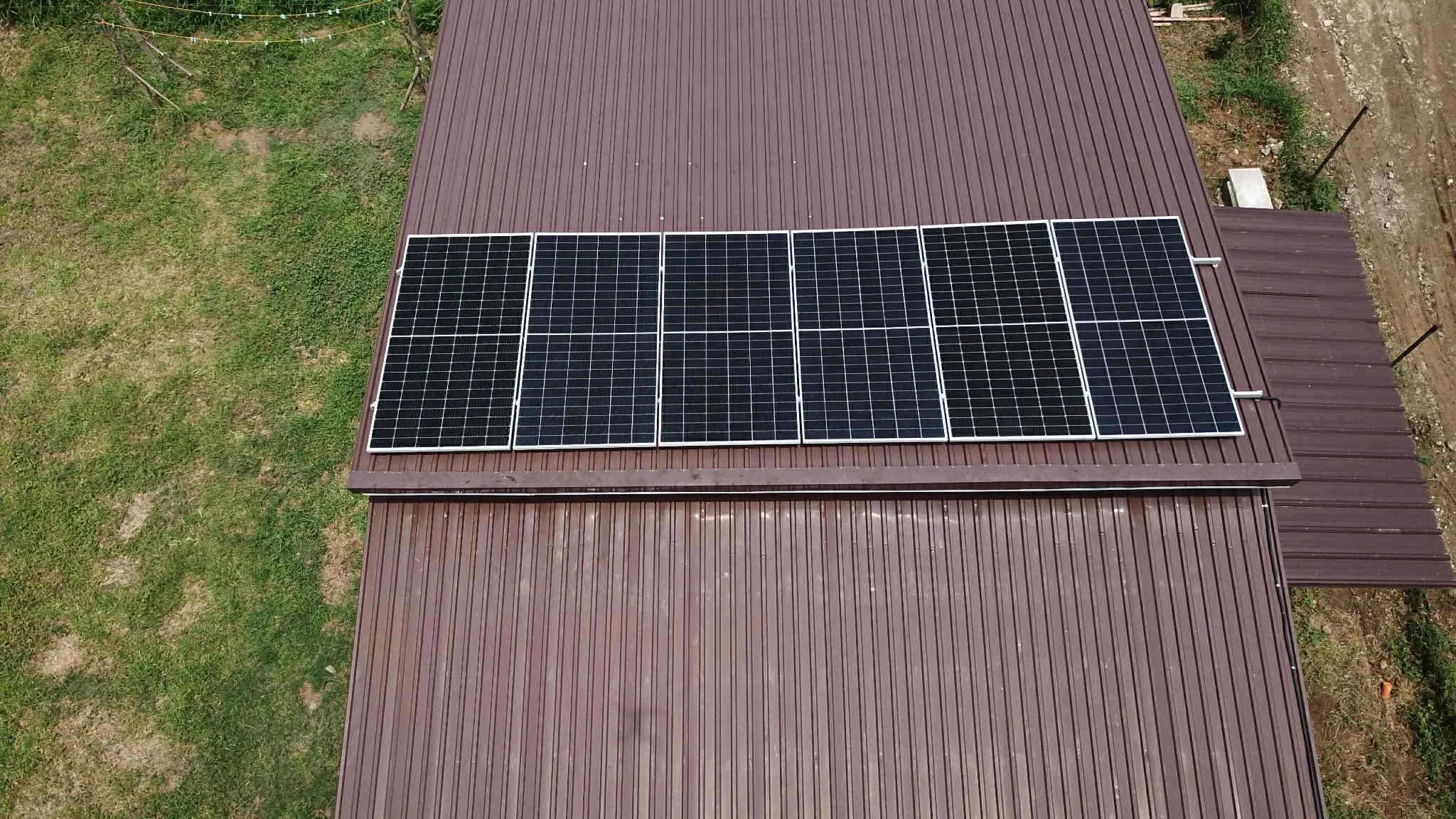 Aerial view of a building with a brown metal roof fitted with eight solar panels arranged in two rows of four panels each.