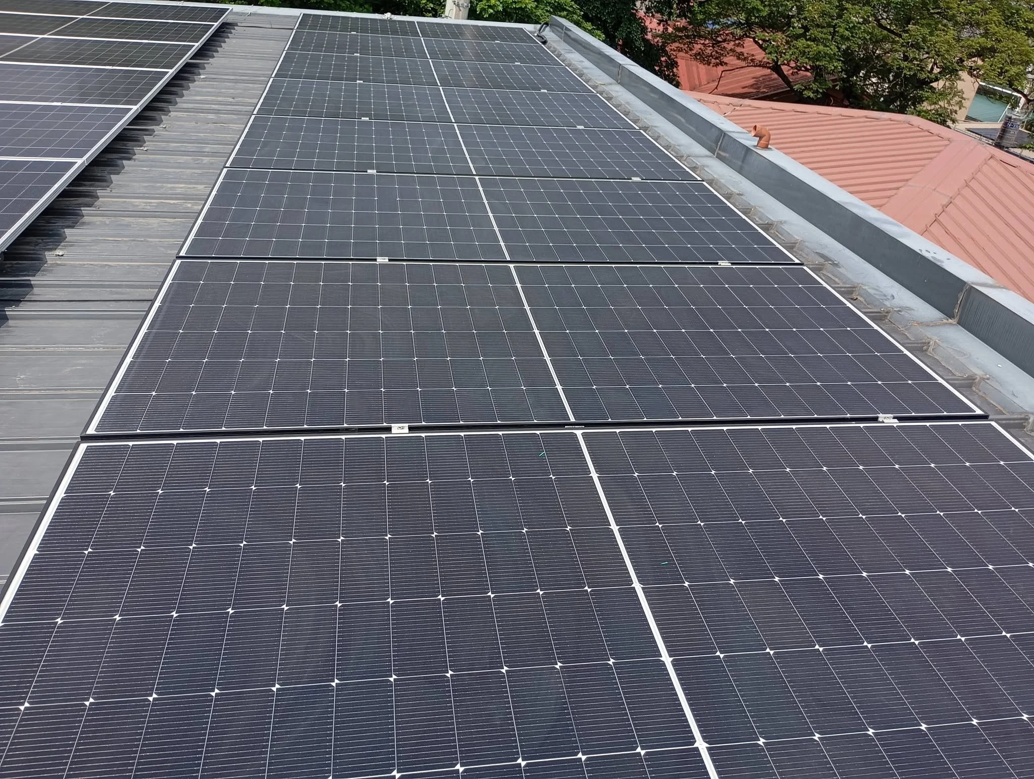 Multiple solar panels installed on a building's roof with trees in the background.