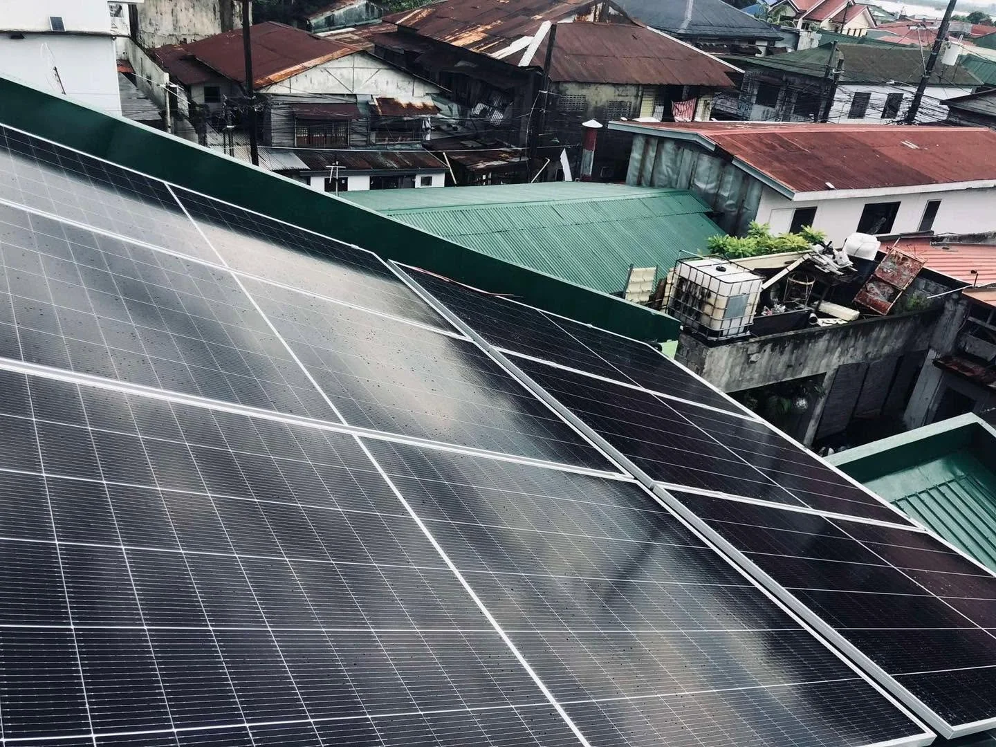 Solar panels installed on a rooftop in a residential area with neighboring houses and rooftops visible.