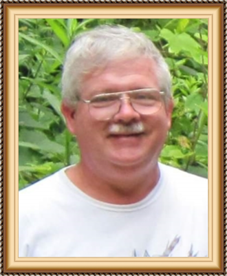 A smiling man with gray hair, glasses, and a mustache standing outdoors in front of green foliage.