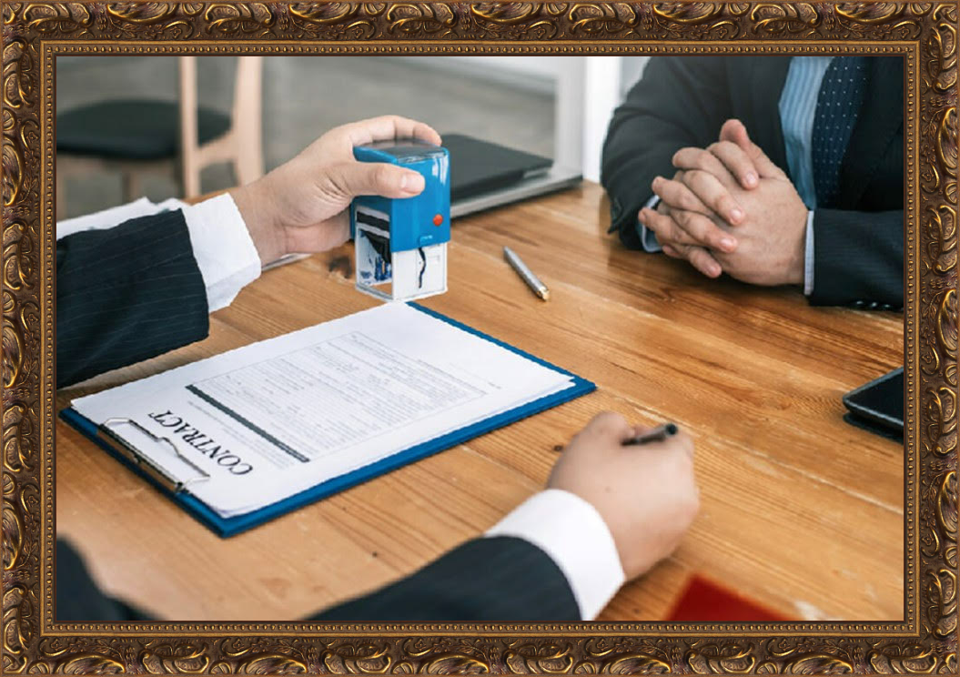 Two individuals in a business setting during a job interview or meeting. One person is stamping a document labeled 'CONTRACT' while the other person is sitting with hands clasped on the table. The table has a pen and some folders or papers.