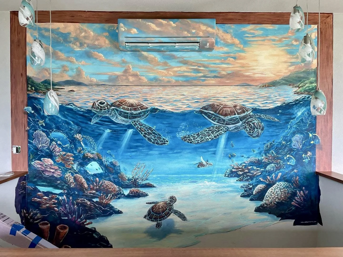 Mural of an ocean scene with turtles swimming near coral reefs and rocks, with a sunset sky above.
