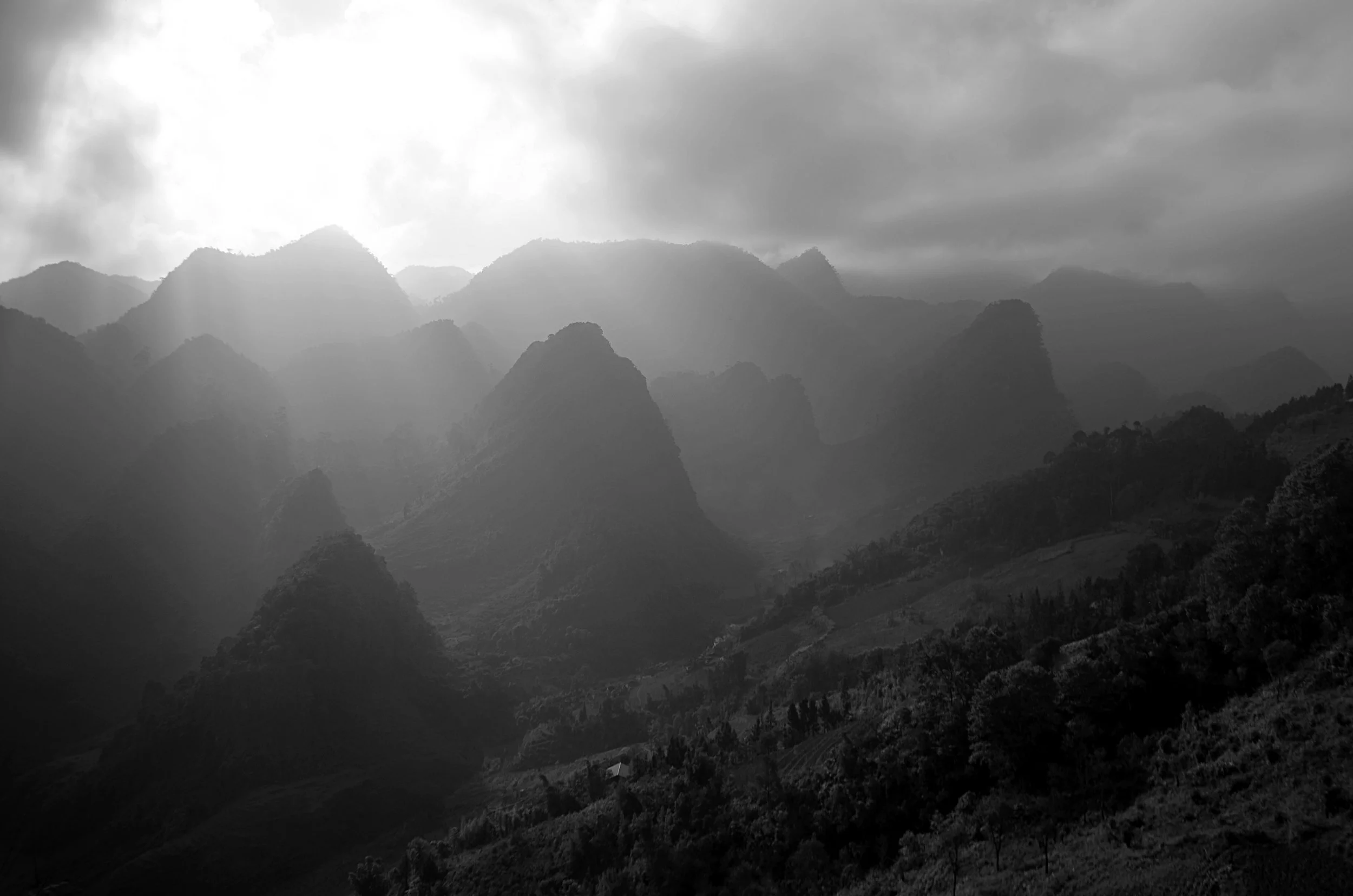 Black and white photograph of a mountain landscape with multiple ridges and valleys, cloudy sky overhead.