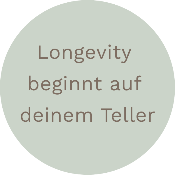 Ein kreisförmiges, hellgraues Schild mit dem deutschen Text 'Langlebigkeit beginnt auf deinem Teller'.