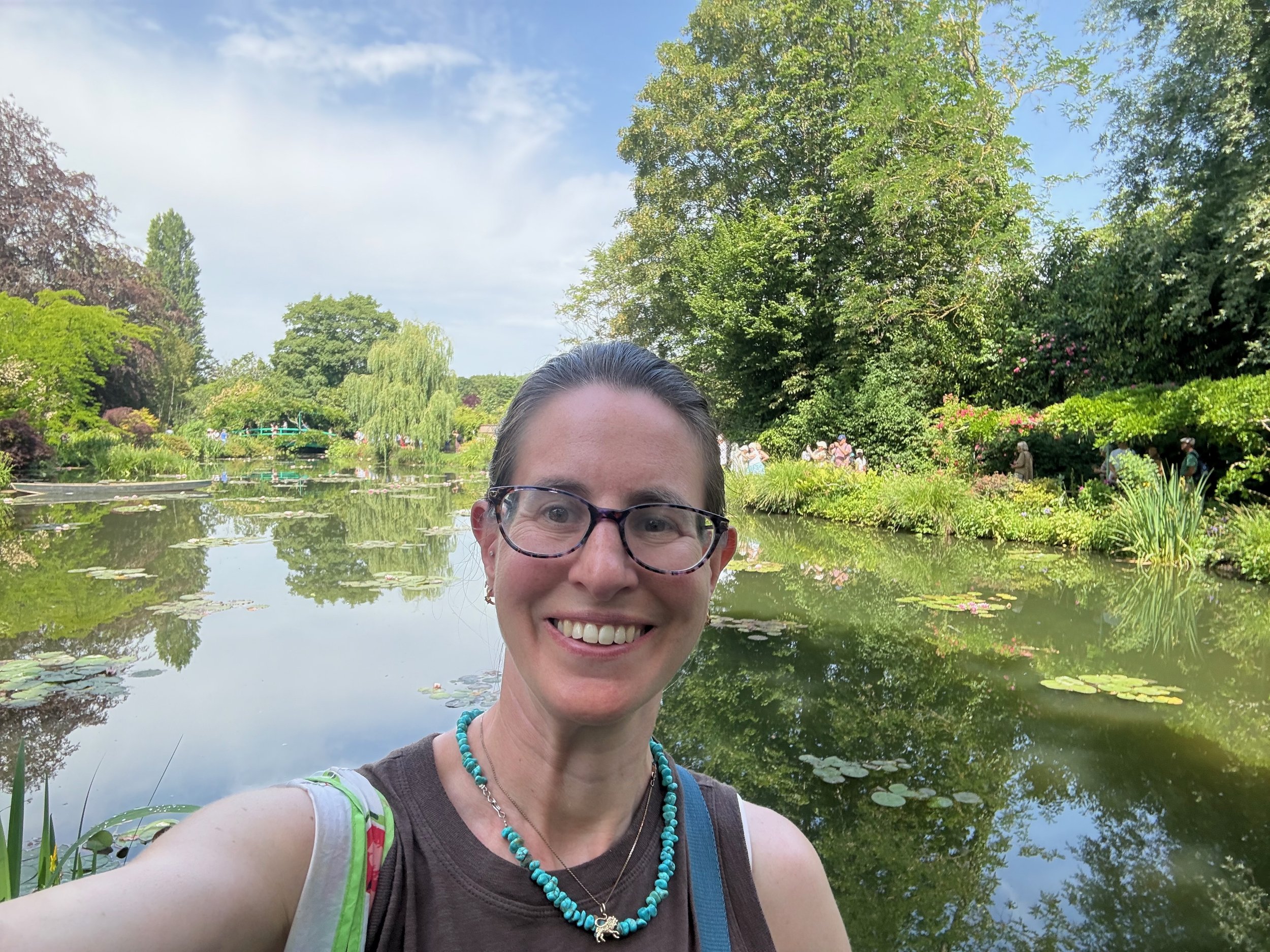 A woman smiling in front of a pond with water lilies symbolizing joy and expansiveness, exploration, and curiosity