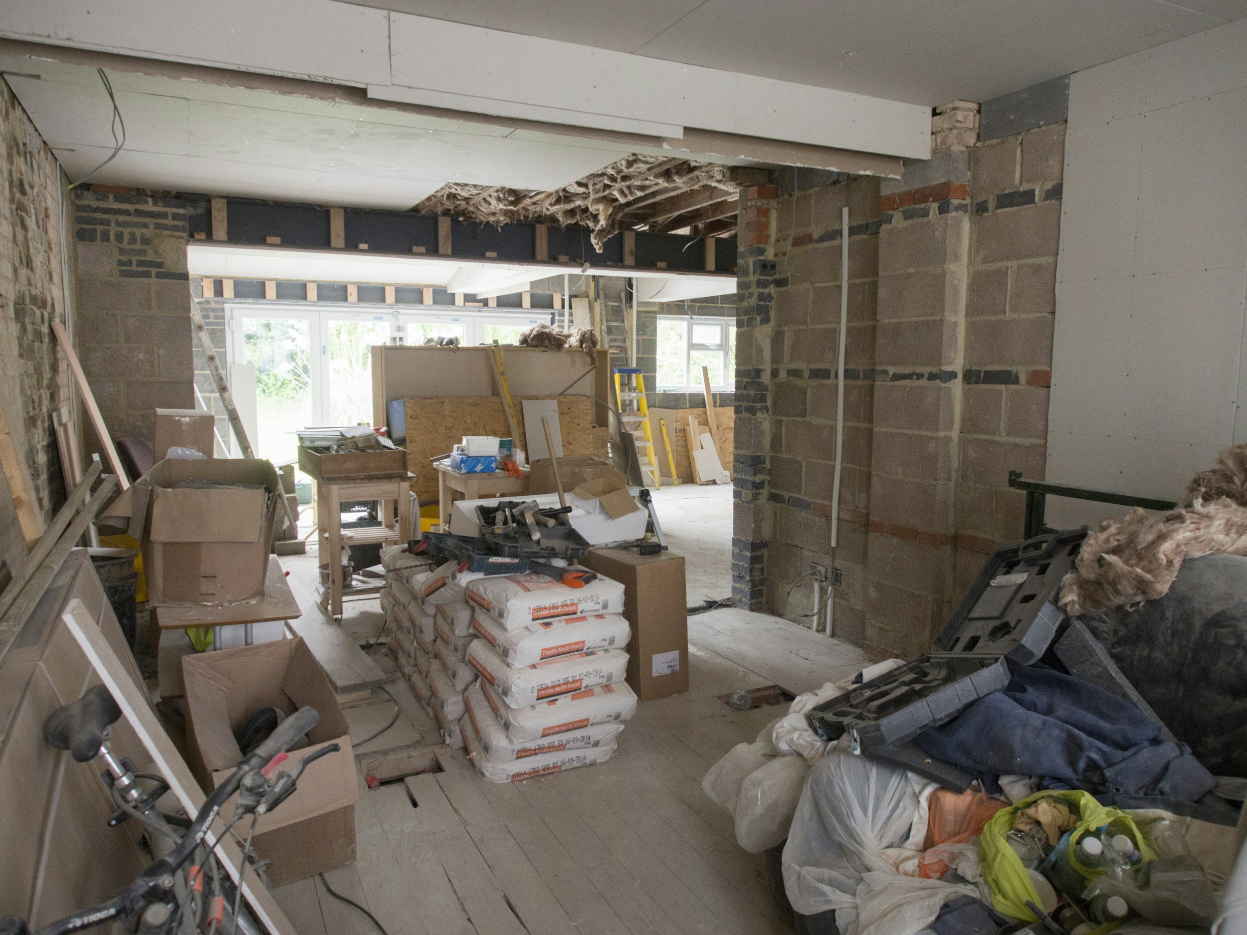 Interior of a house under construction with exposed brick walls, construction materials, and tools scattered around.