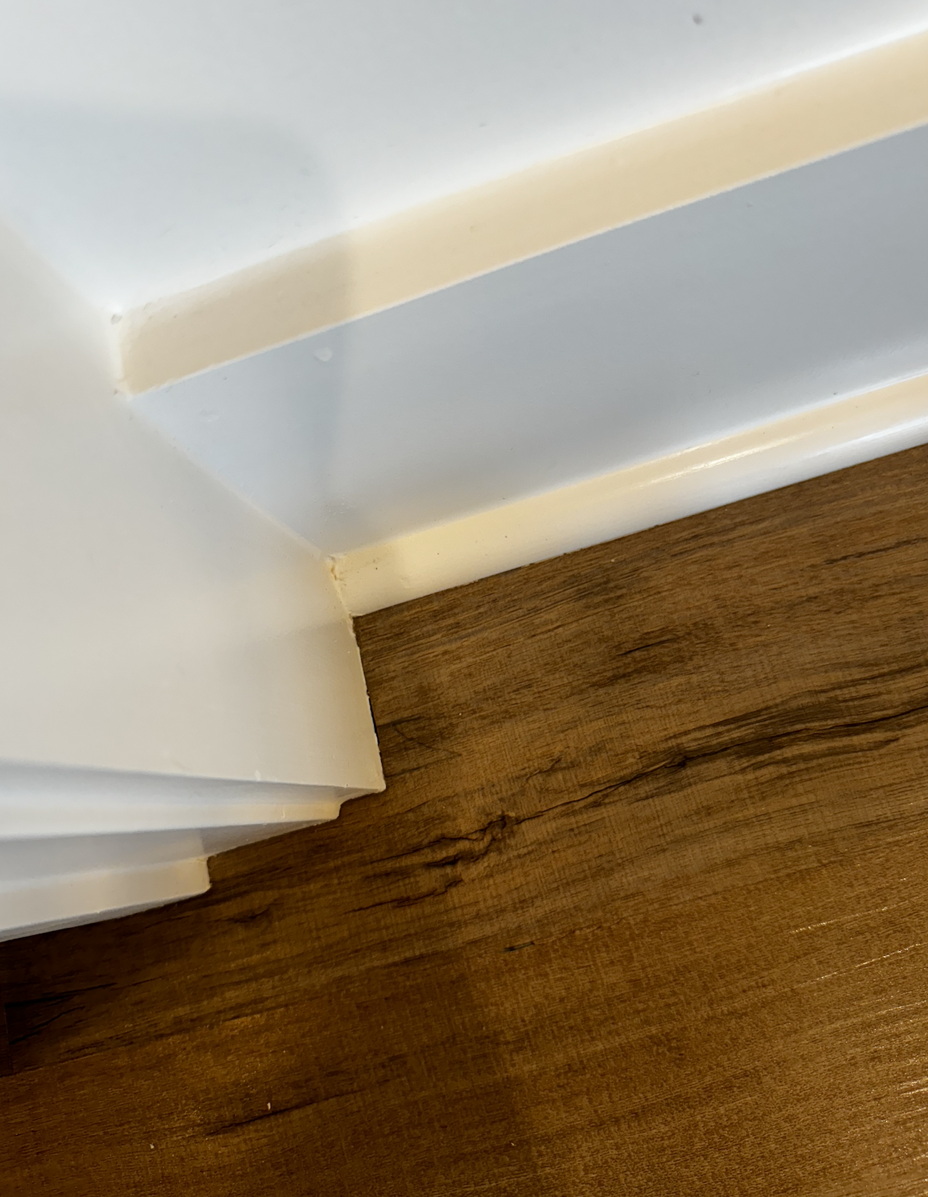 Close-up of a white chair or furniture corner next to a wooden floor.