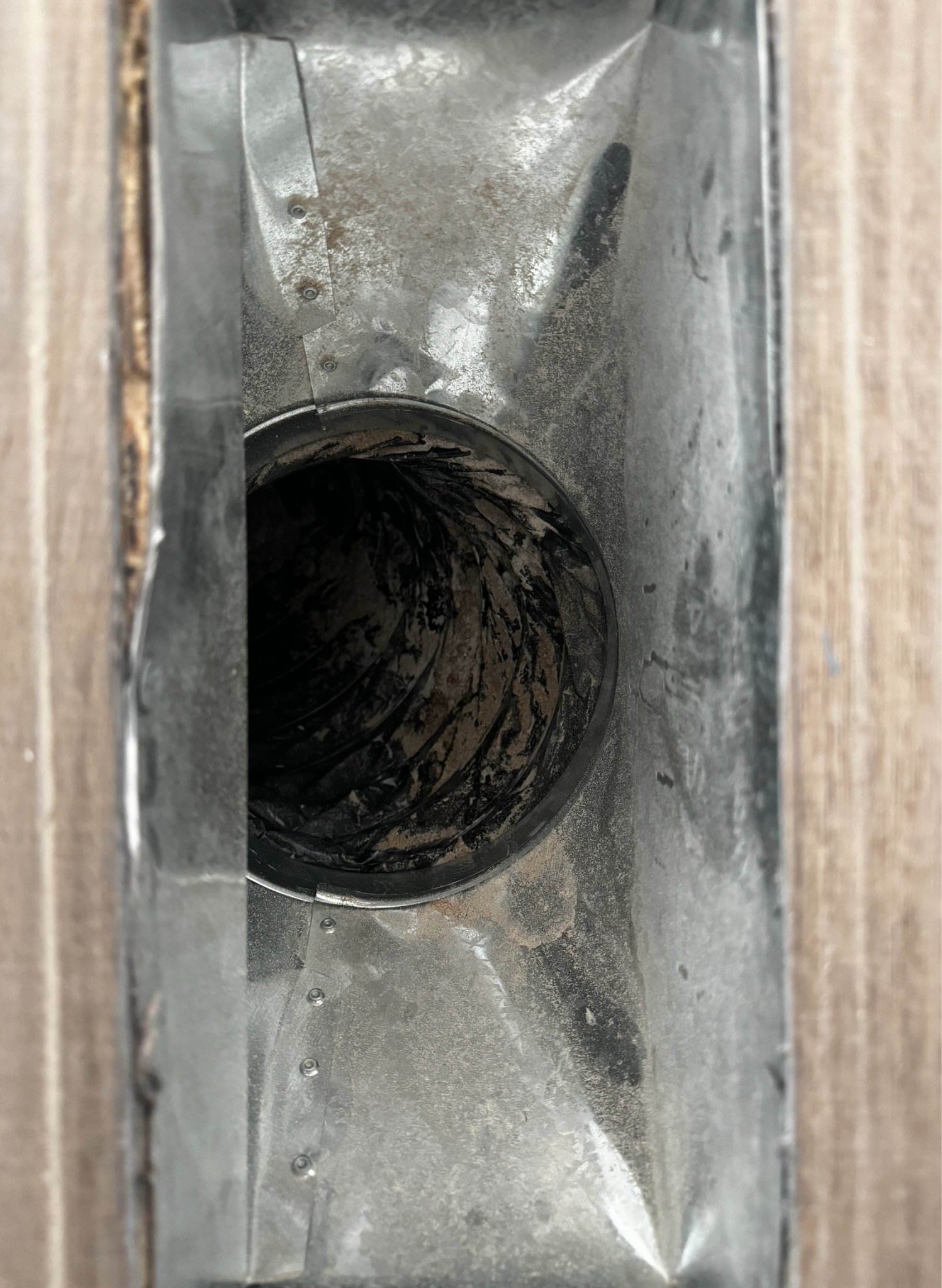 Close-up image of a metallic chimney vent with soot and debris inside, viewed from above.