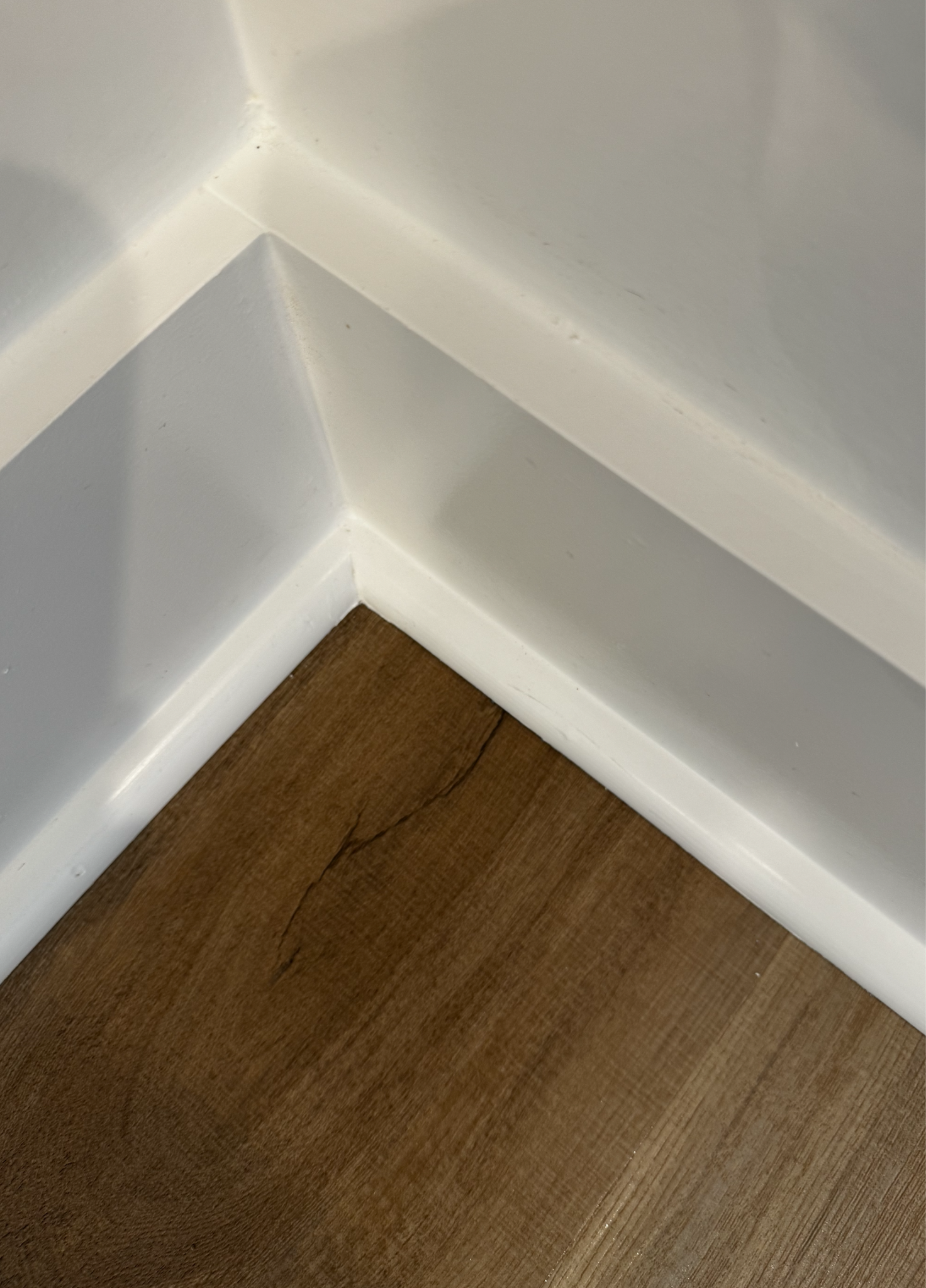 Close-up of a white wall with trim and brown hardwood floor.