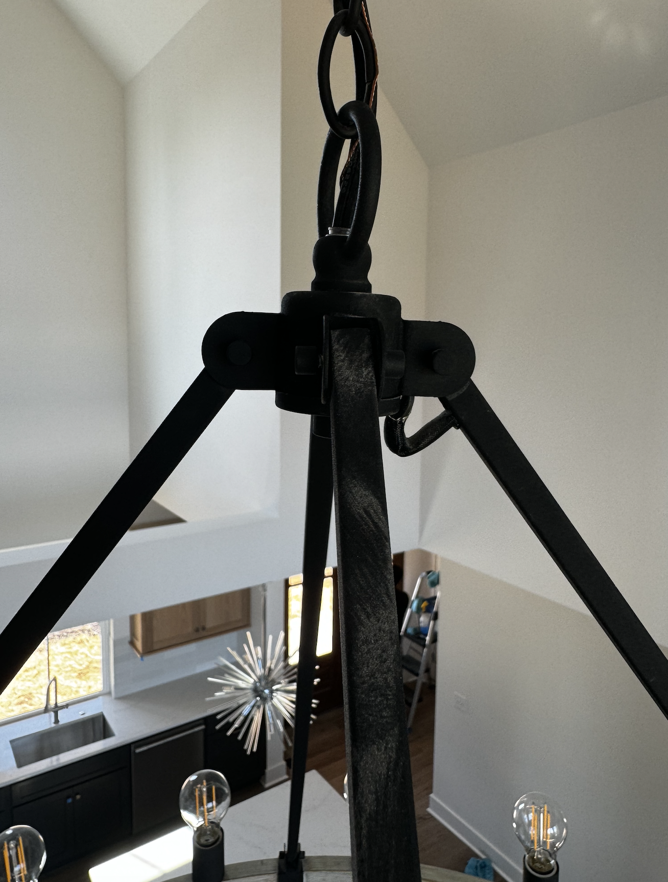 Close-up of a black metal chandelier with Edison-style light bulbs hanging from a ceiling in a modern home interior.