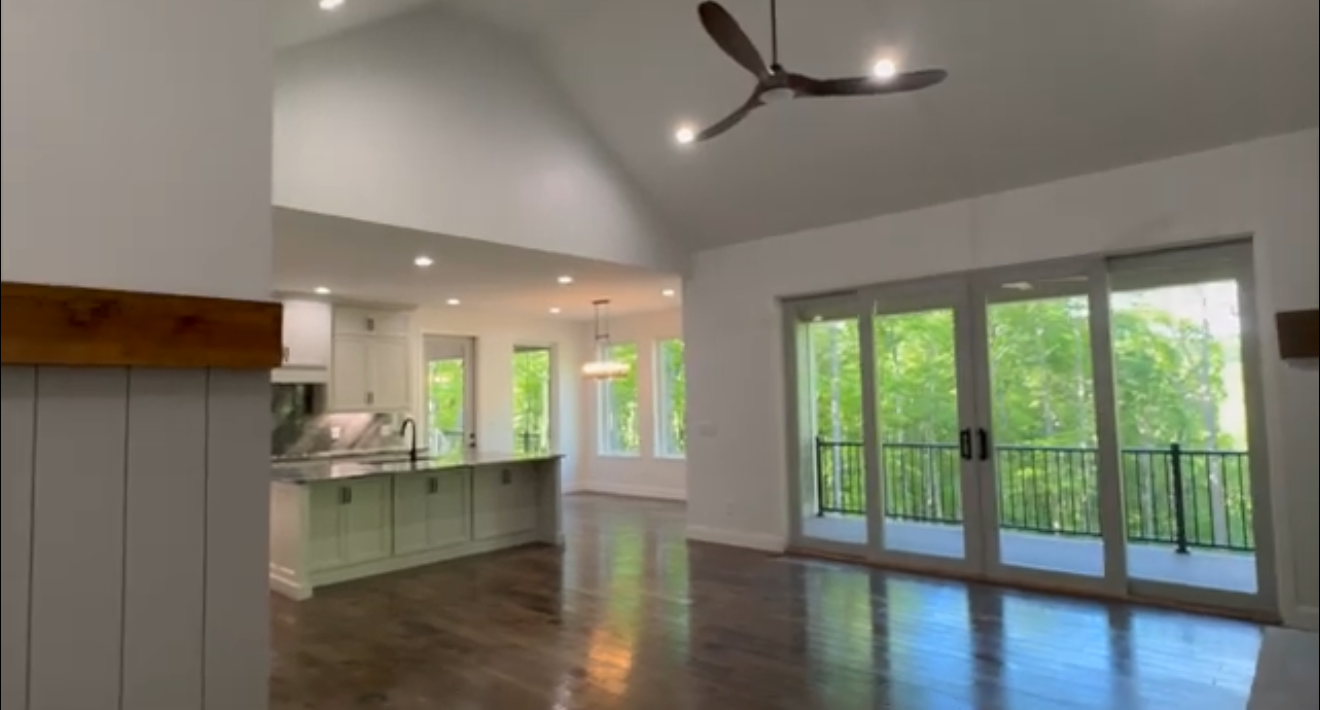 Interior of a modern living space with hardwood floors, large windows, a kitchen with a breakfast bar, and a balcony with sliding glass doors leading outside.