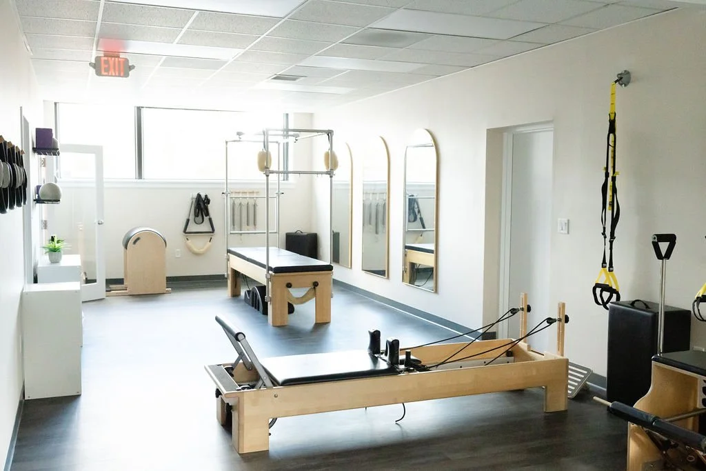 Pilates studio with a reformer, mirrors, hanging straps, resistance bands, and exercise balls