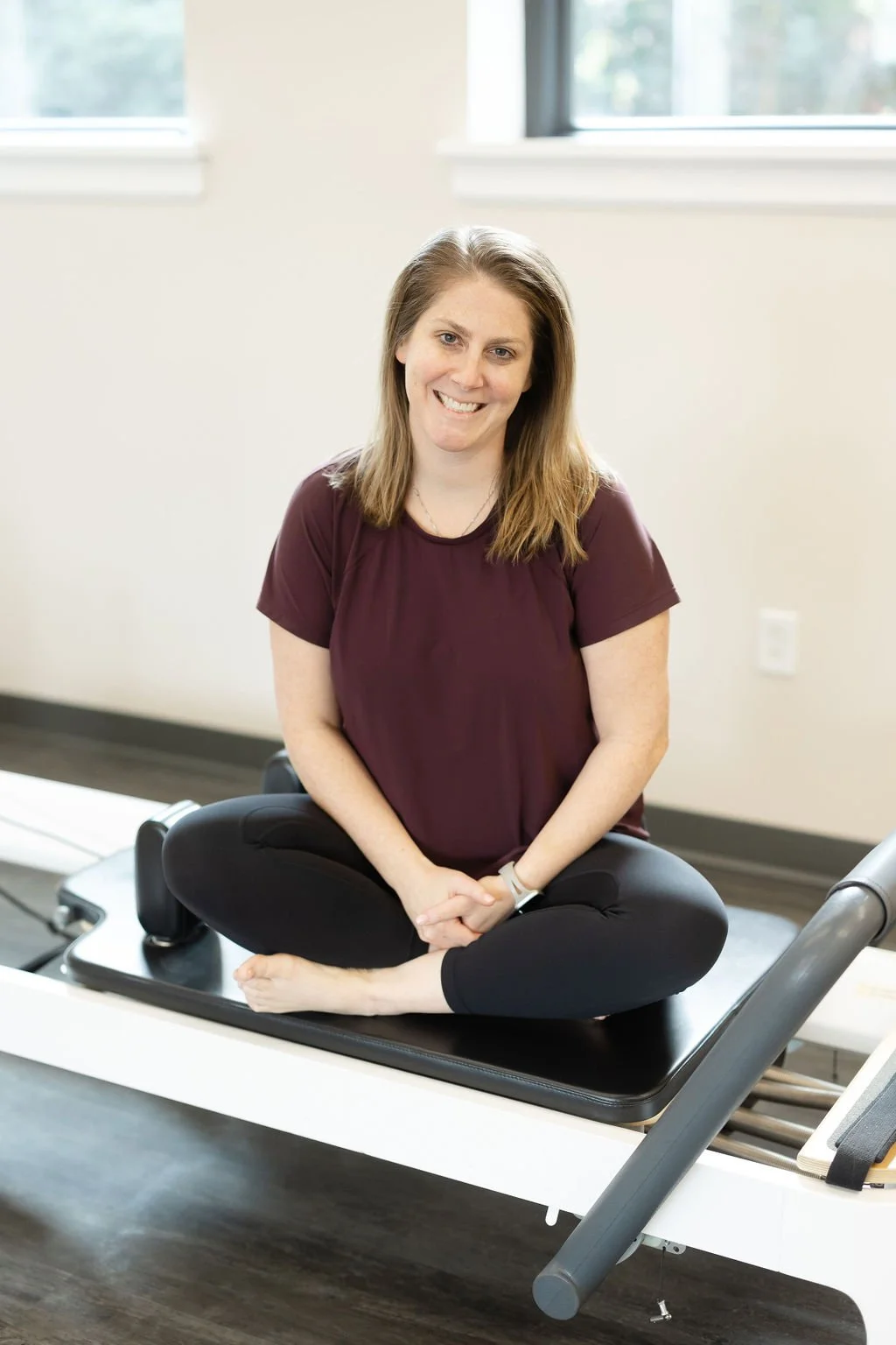Dara Galasso sitting cross-legged on a reformer, smiling in the studio.