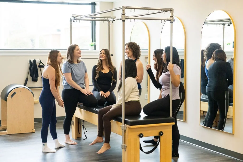 A group of clients in a Pilates class engaging in a discussion in the studio