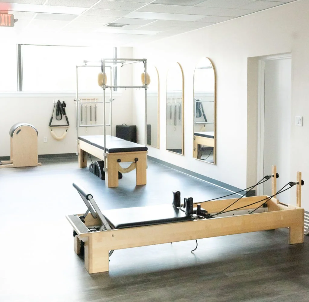 Pilates studio with reformers, mirrors, and equipment in a well-lit room