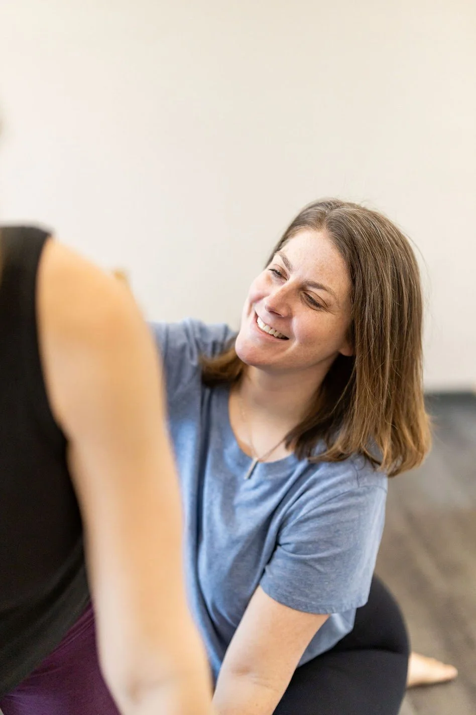 A client in a blue t-shirt smiling while stretching with another person during a Pilates session in the studio