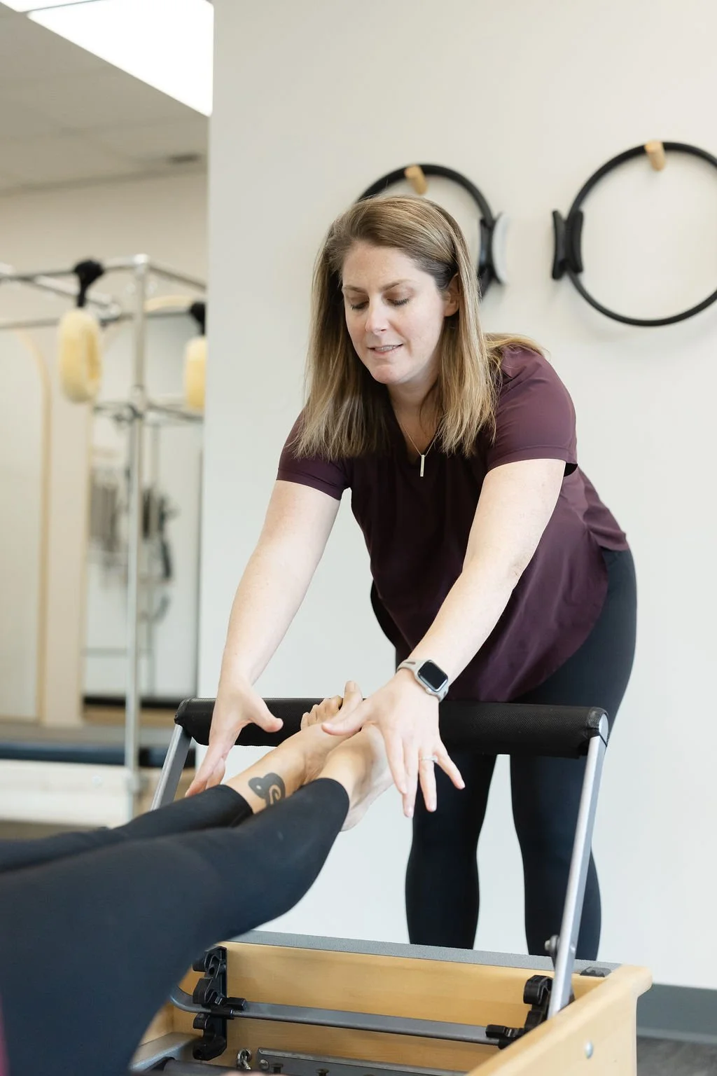 Instructor assisting a client during a Pilates session, with Pilates equipment visible in the background