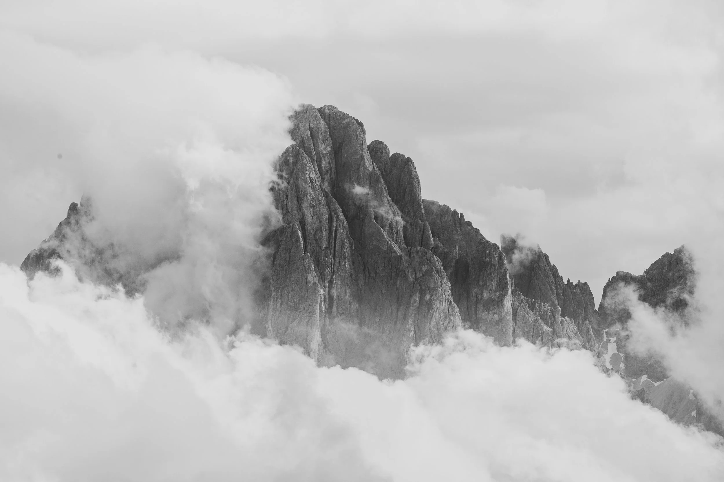 Black and white photograph of jagged mountain peaks surrounded by clouds.