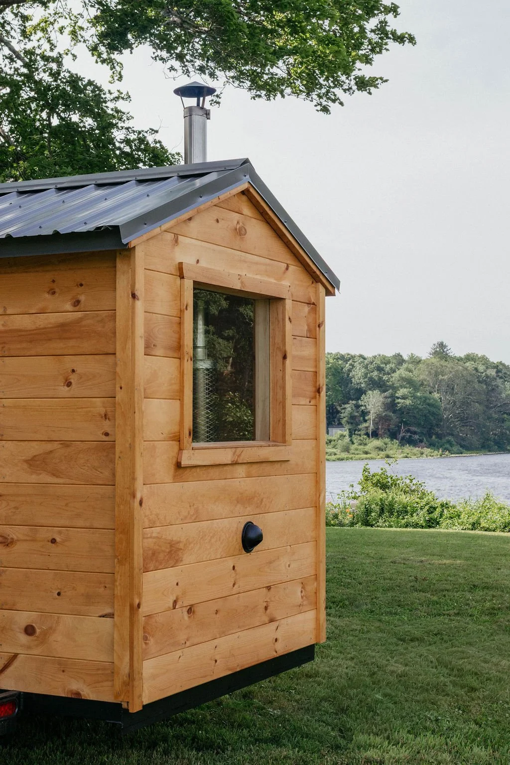 Small wooden cabin with a metal roof, near a lake, with trees in the background.