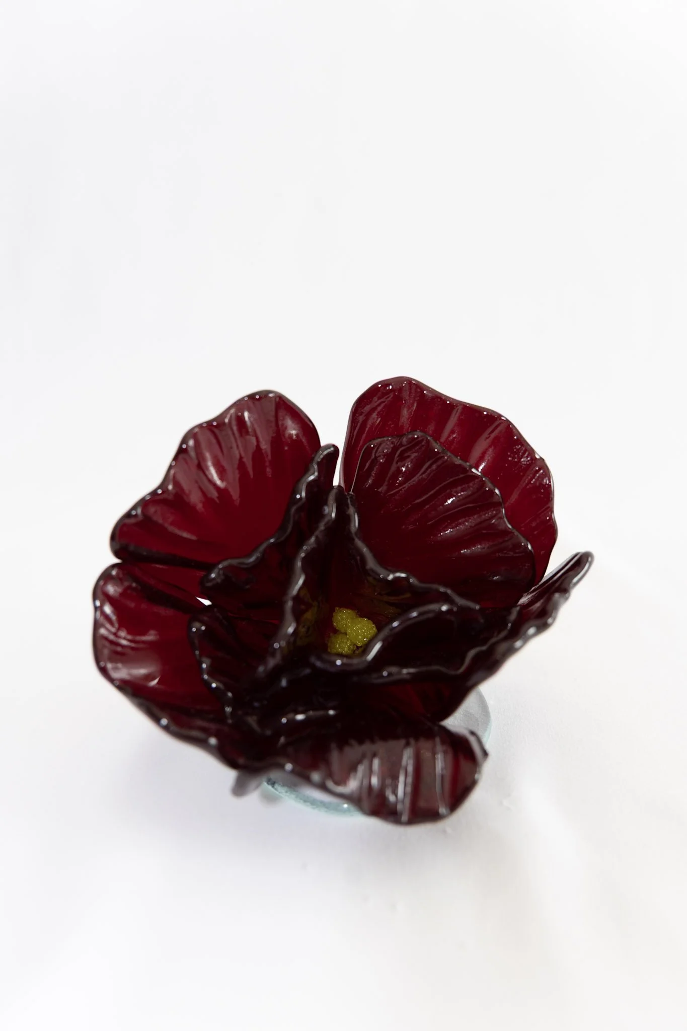 Red and black glass flower sculpture with yellow accents on a white background.