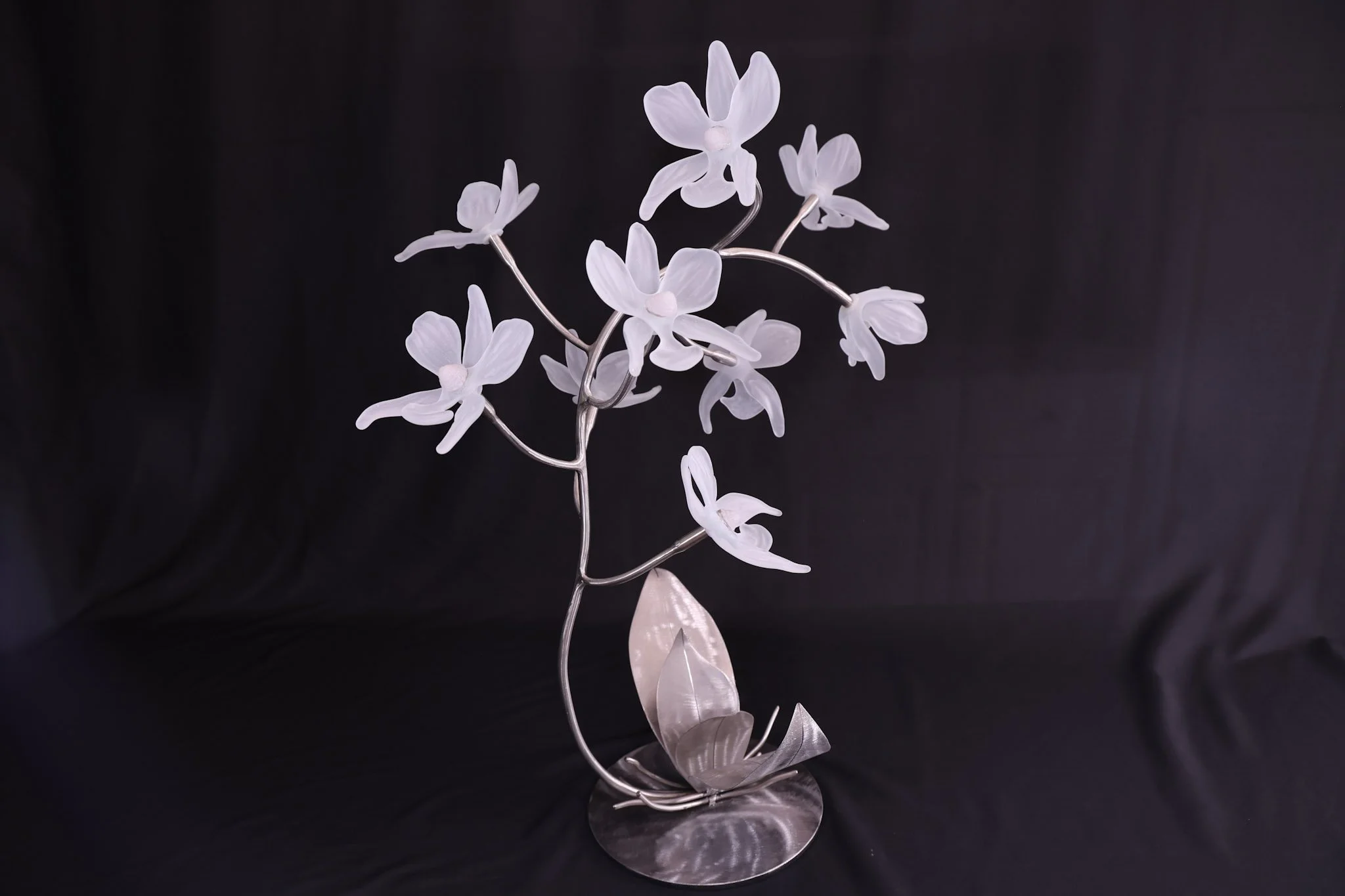 Elegant silver and white floral sculpture resembling orchids on a dark background.