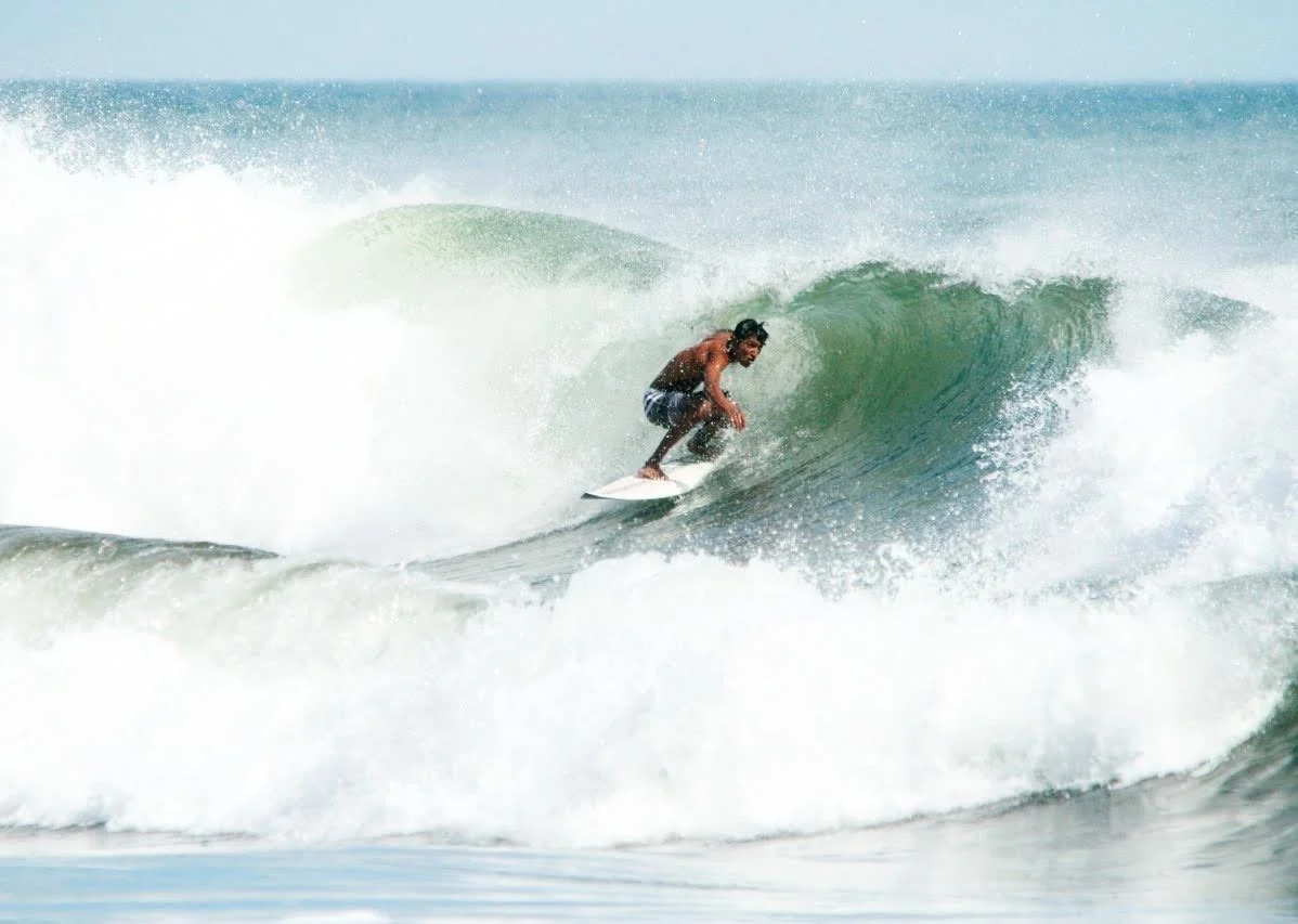 Surfer riding inside a green ocean wave with white foam.