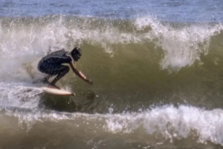 Person in a wetsuit surfing on a wave at the beach.