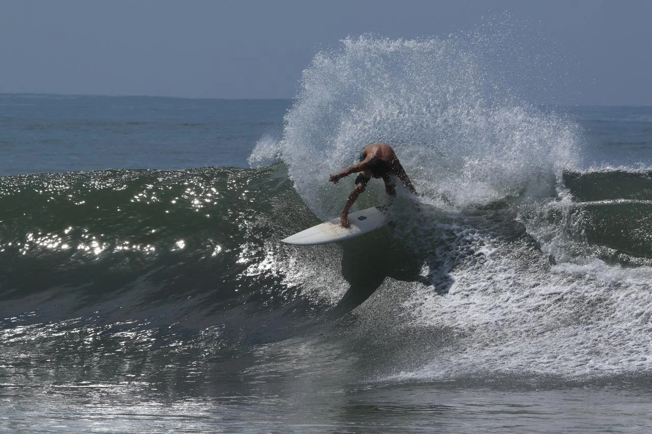 A person surfing on a wave in the ocean wearing black shorts, with spray of water around.