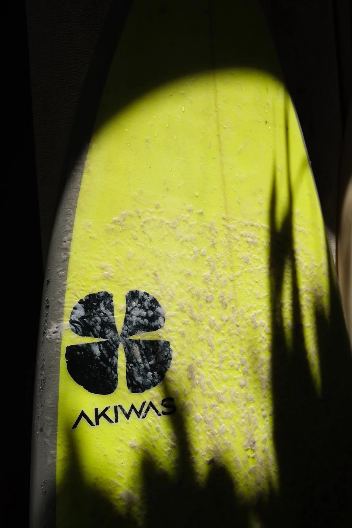 Close-up of a yellow object with black logo and the word 'AKIWAS,' partially covered in water or soap suds, with shadows cast over it.