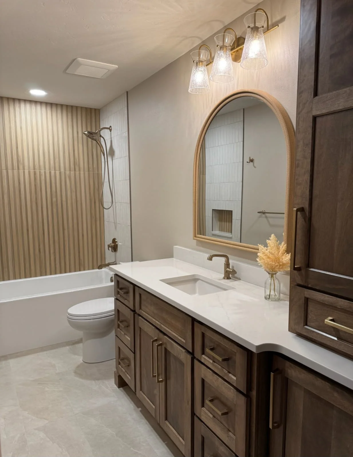 Bathroom with a vanity, mirror, and light fixture, with a bathtub and shower area in the background.