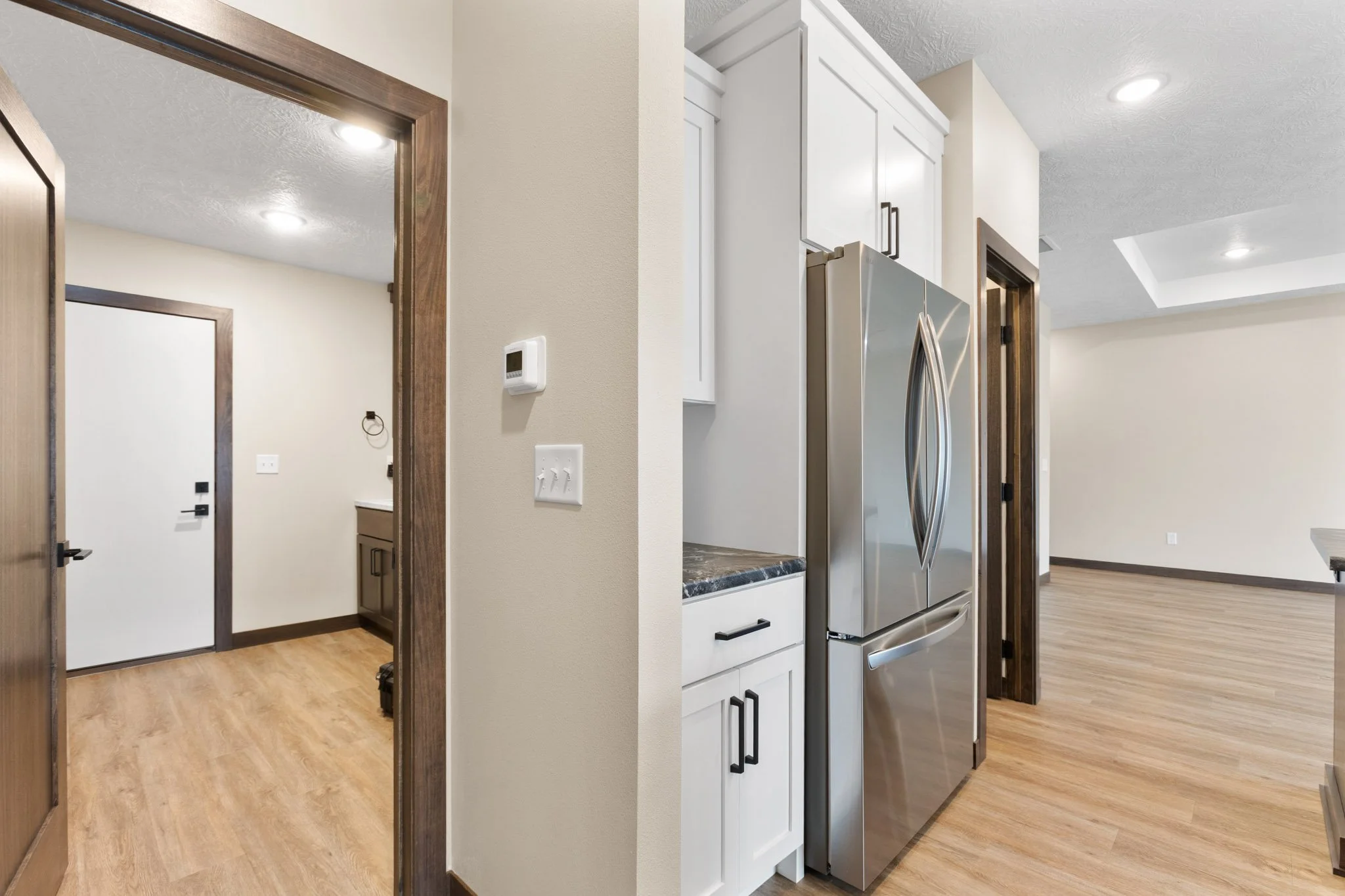 Modern kitchen with white cabinets, stainless steel refrigerator, wood flooring, and beige walls.