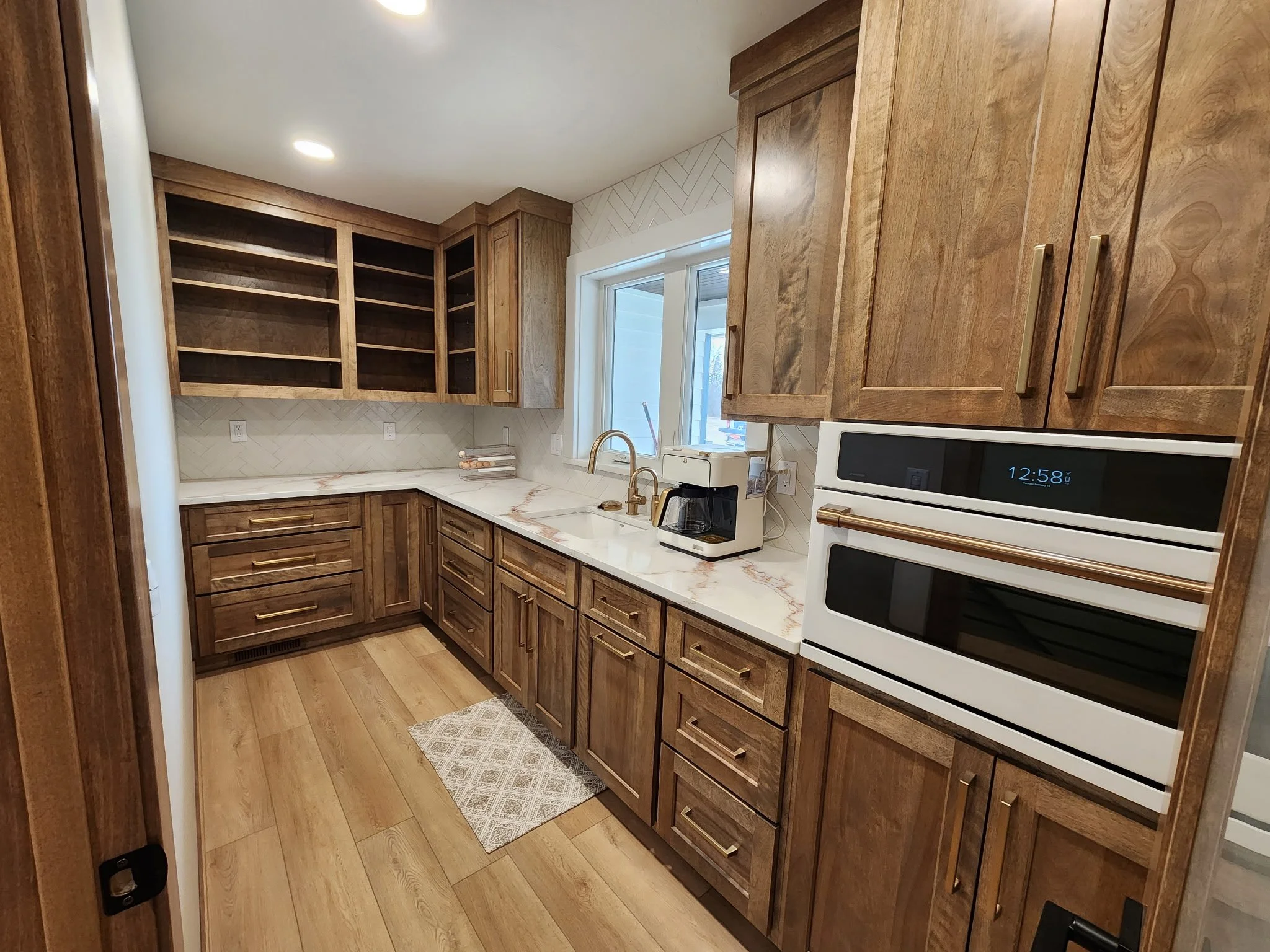 Kitchen with wooden cabinets, a marble countertop, and a window. There is a coffee maker and microwave on the counter, and a small mat on the floor.