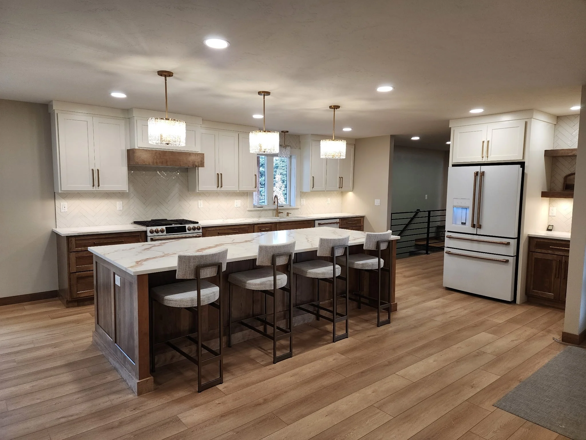 Modern kitchen with white cabinets, marble island, pendant lights, and hardwood floors.