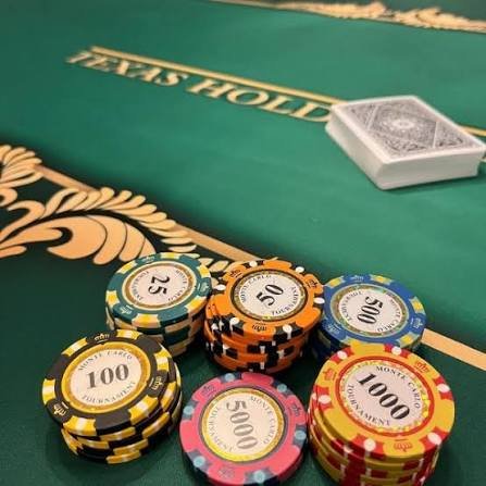 Casino poker chips with denominations ranging from 25 to 10,000 placed on a green poker table with a deck of cards in the background.