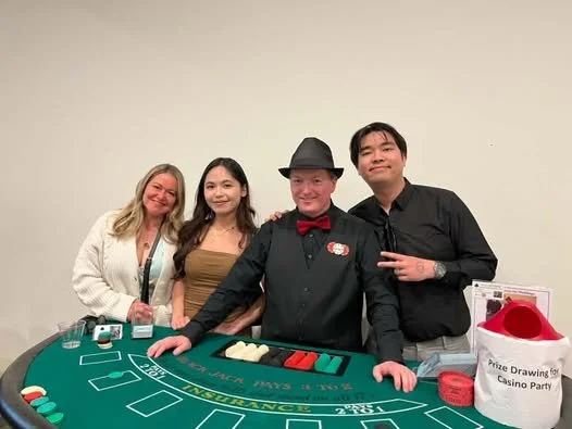 Four people posing behind a casino table at a casino-themed event.