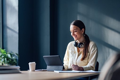 Woman with headphones smiling at a laptop in a modern office