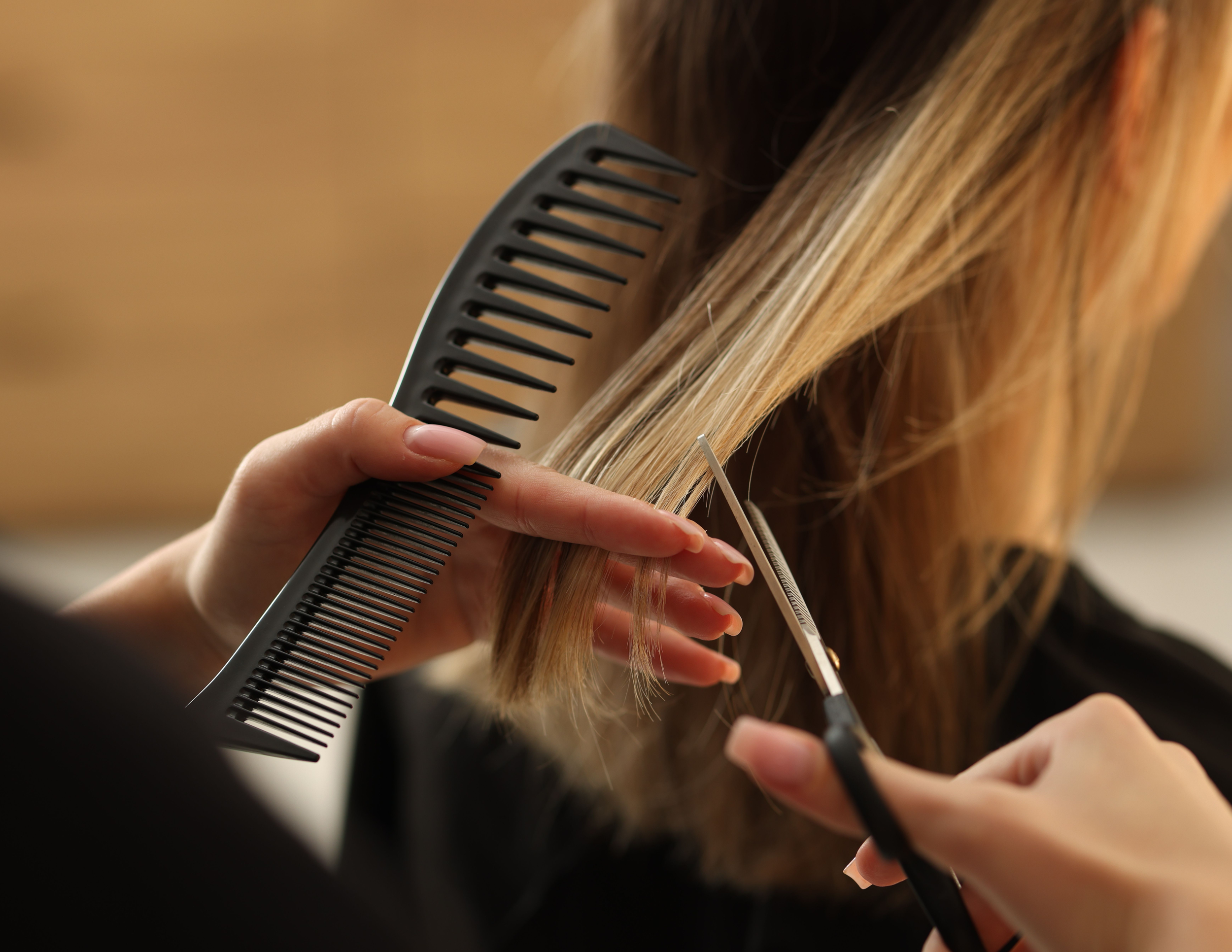 A person is holding a black hair pick comb and a pair of scissors while cutting long blonde hair.